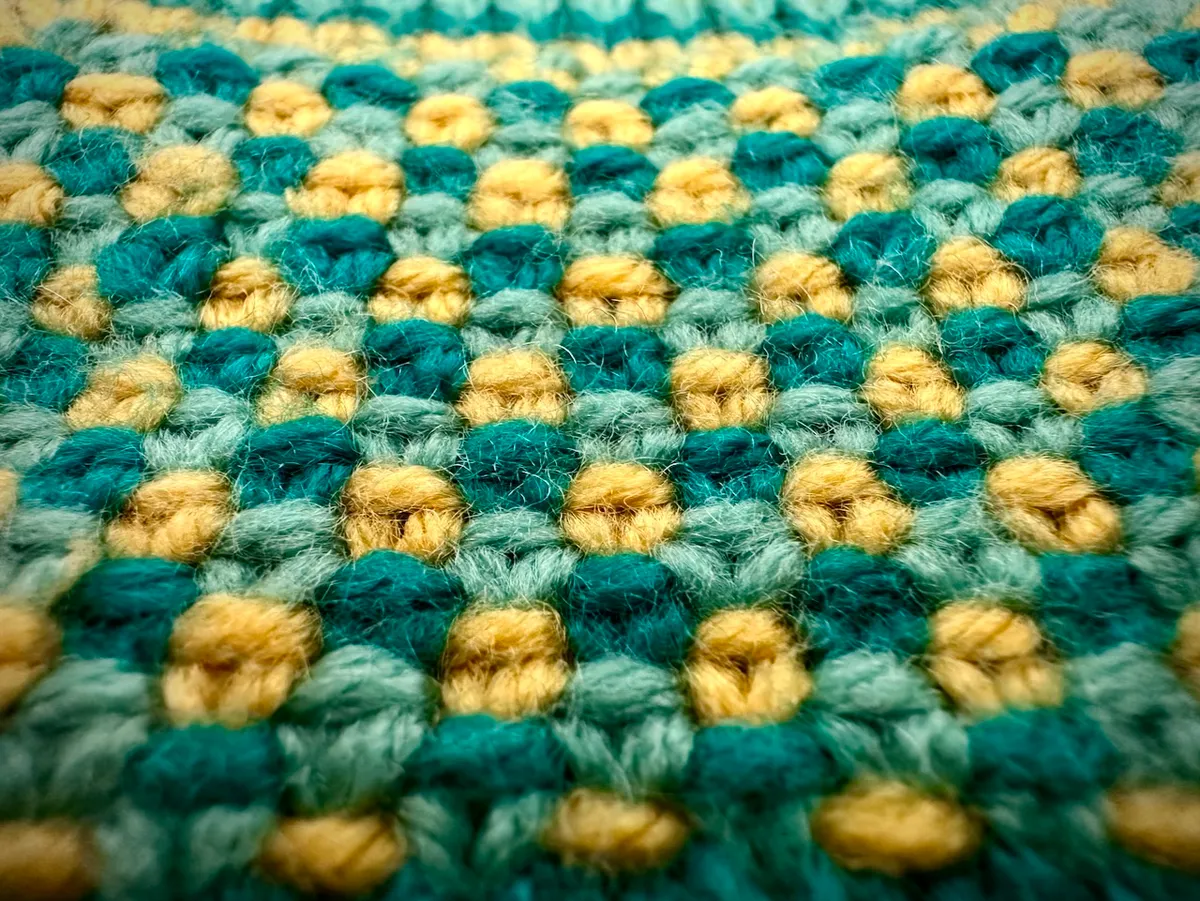 Closeup of a three-color handknit swatch in alternating triangular patches of yellow, green, and turquoise.